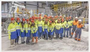 Gruppebilde av elevar i besøkfrakk og hjelm på besøk hos bedrifta Hydro Recycling